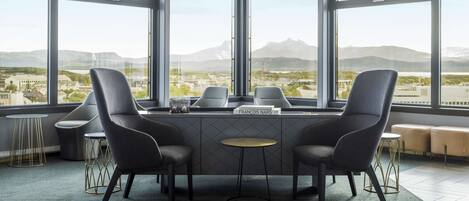A modern meeting room with a large table, four chairs, and a view of a cityscape through large windows.