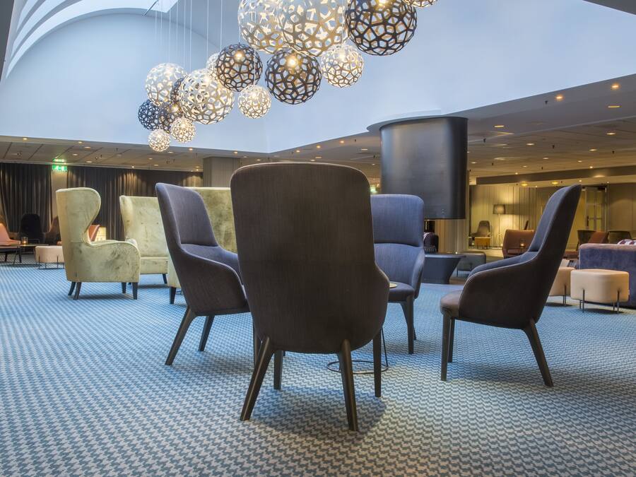 A modern lobby with patterned carpet, contemporary chairs, and a unique ceiling light fixture.