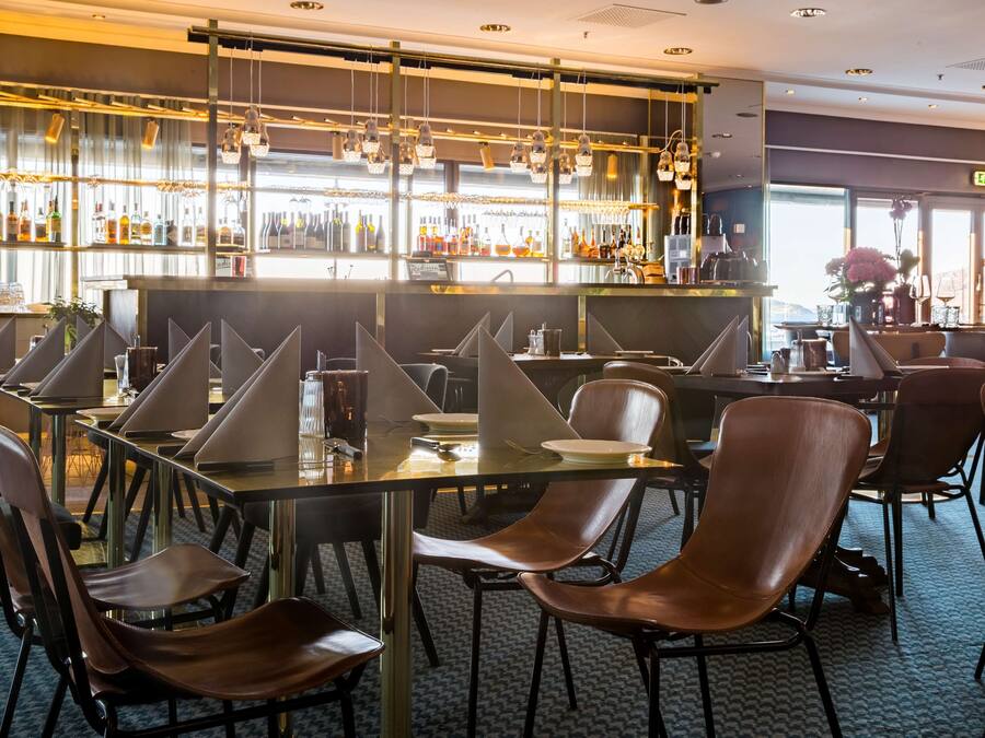 Un espace bar doté de nombreuses tables et chaises, d’un comptoir bien garni et offrant une vue sur l’extérieur grâce à de grandes fenêtres.