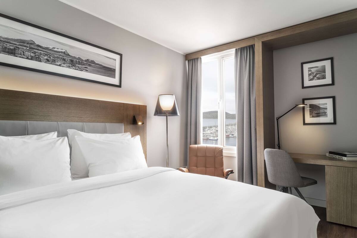 Habitación de hotel con una cama grande, un escritorio, una silla y una ventana con cortinas.