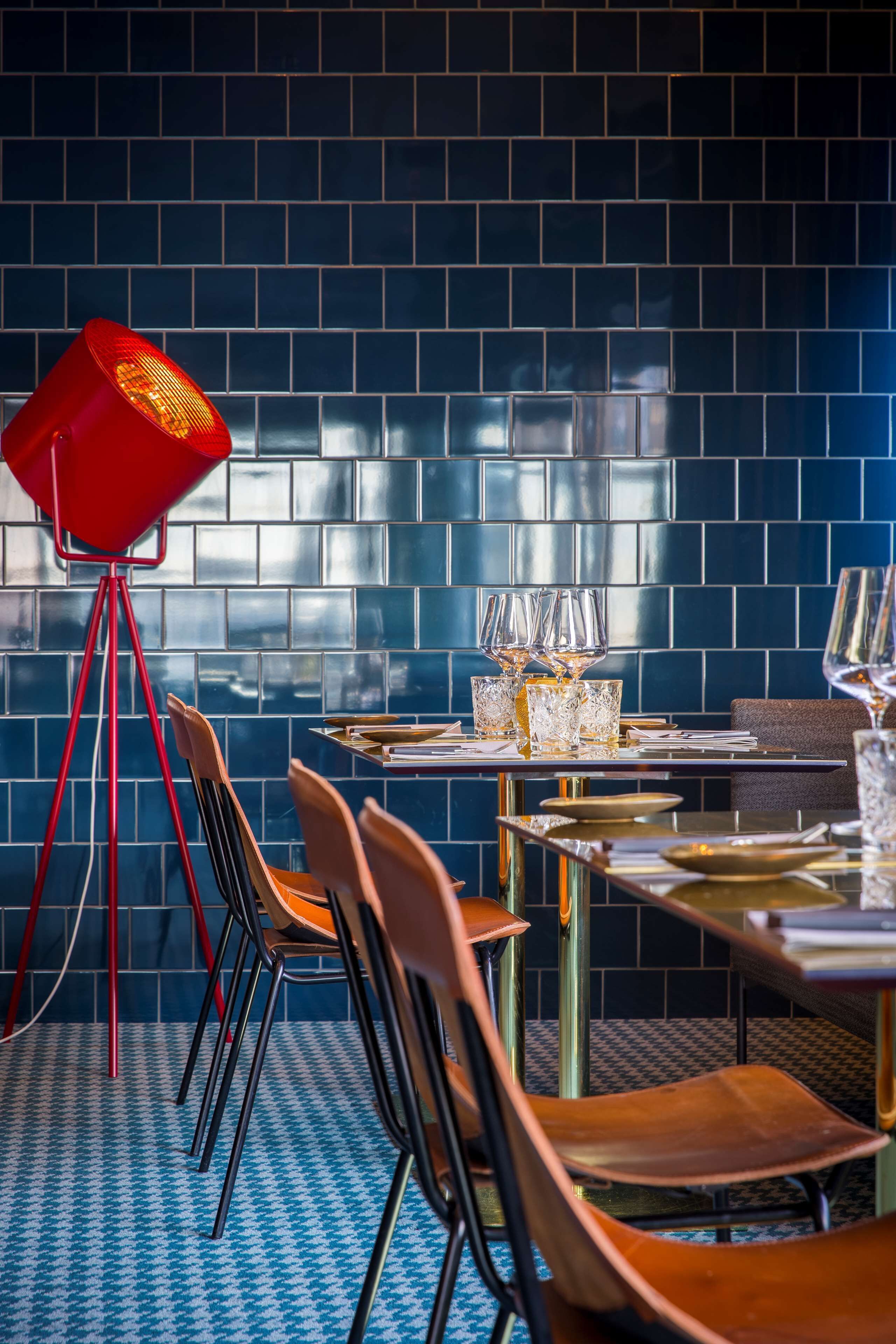A restaurant interior with a blue tiled wall, a red floor lamp, and a table set with glasses and cutlery.