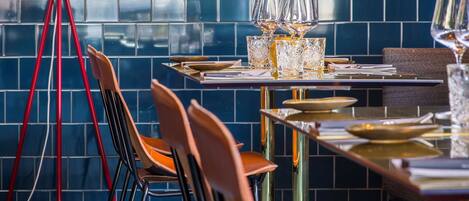 A restaurant interior with a blue tiled wall, a red floor lamp, and a table set with glasses and cutlery.