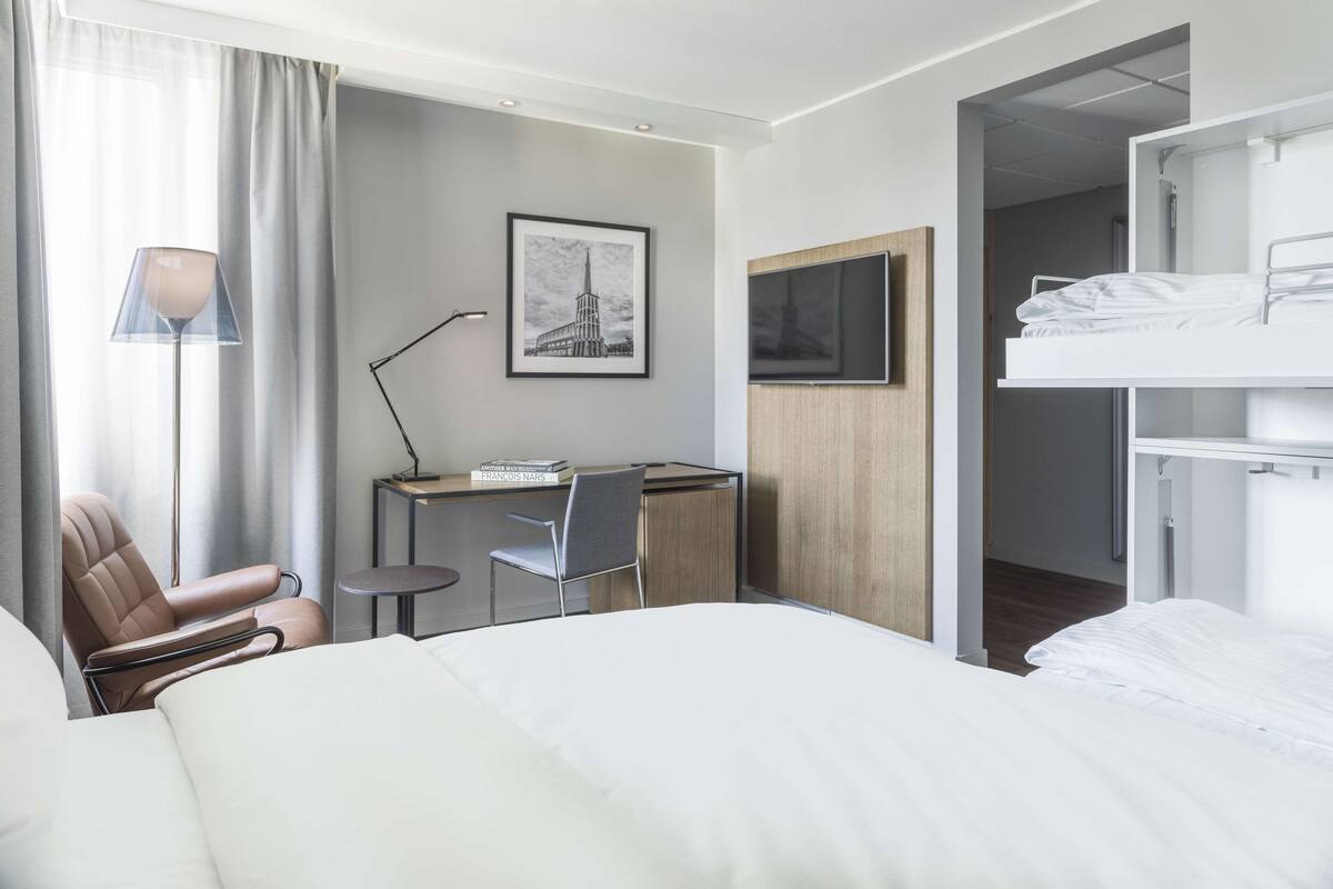 Una habitación de hotel moderna con una cama, un escritorio, una silla, una lámpara y un cuadro en la pared.