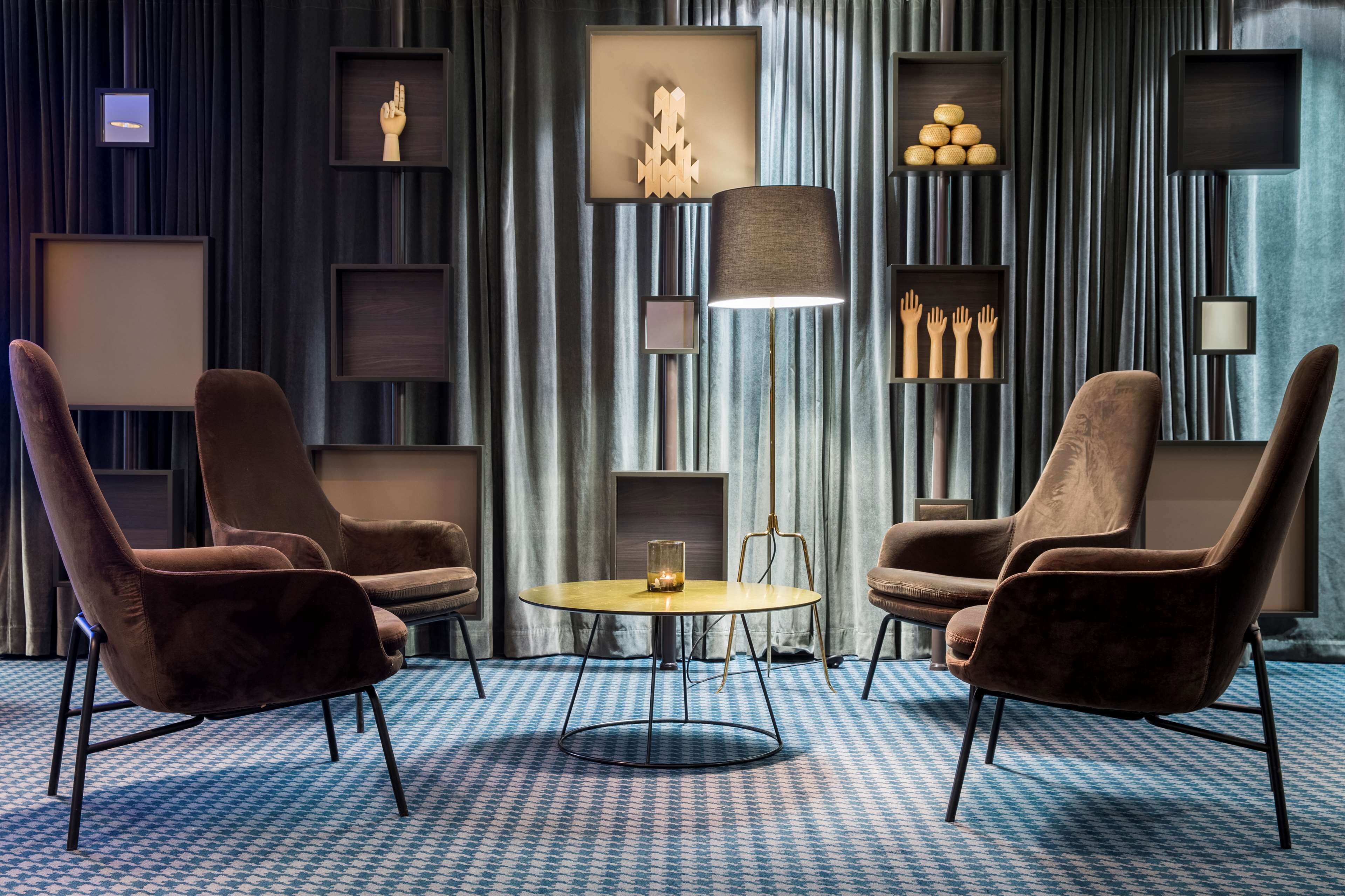 A modern room with two brown armchairs, a round table, and a floor lamp. Shelves with decorative items line the walls.