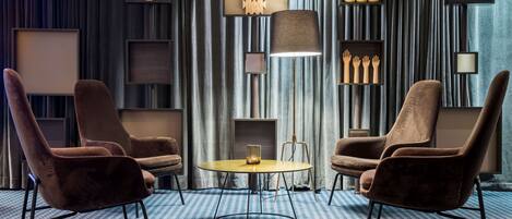 A modern room with two brown armchairs, a round table, and a floor lamp. Shelves with decorative items line the walls.