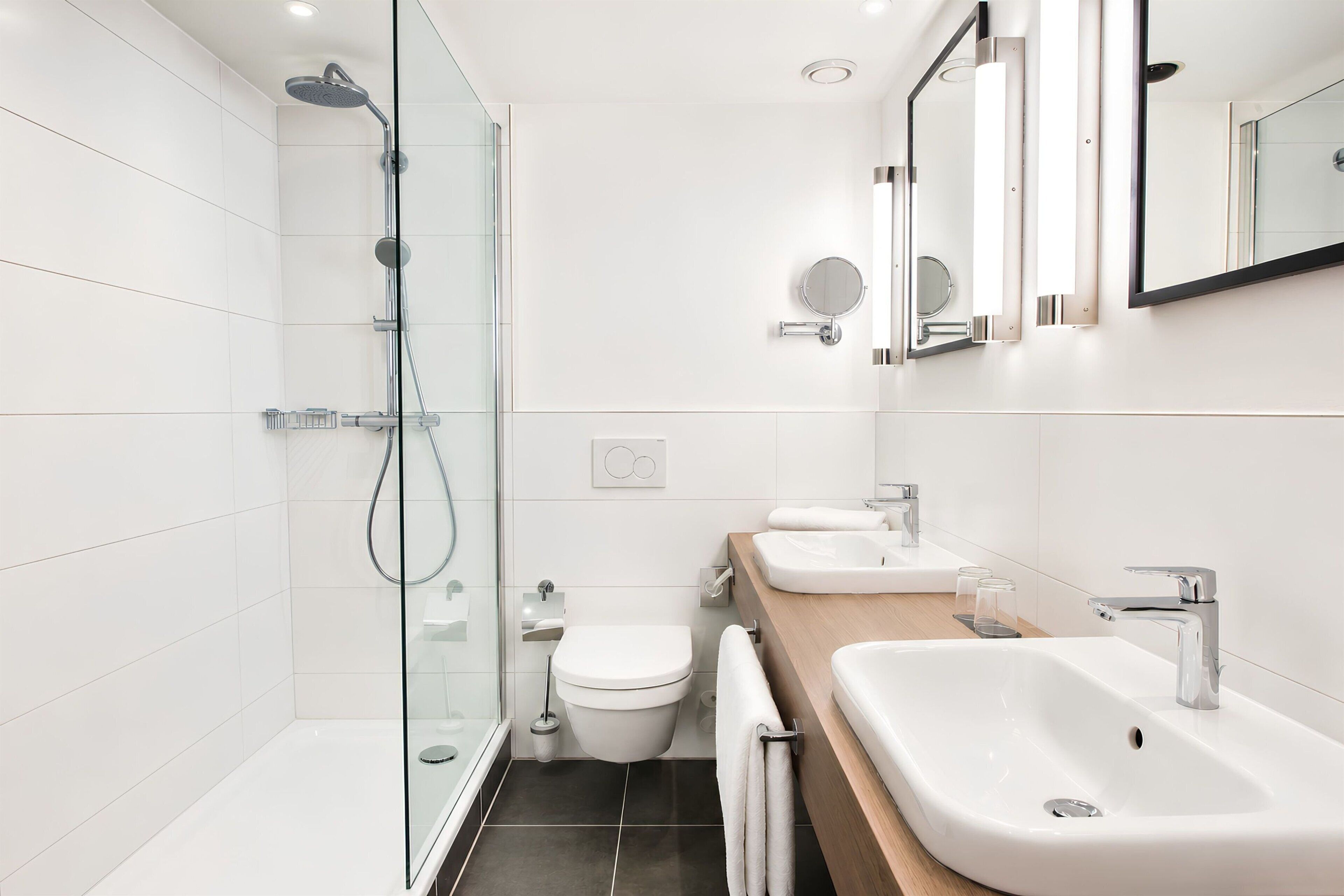 A modern bathroom with a glass-enclosed shower, a toilet, and two sinks with mirrors.