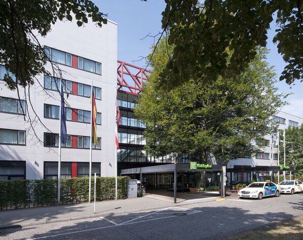 Un edificio moderno de varios pisos, con una estructura metálica roja y el letrero de Holiday Inn.
