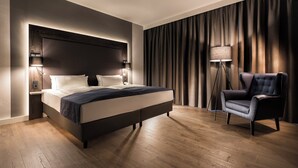 A modern hotel room with a large bed, a dark headboard, two bedside lamps, a floor lamp, and a dark armchair. - Holiday Inn Berlin City West by IHG (Berlin)