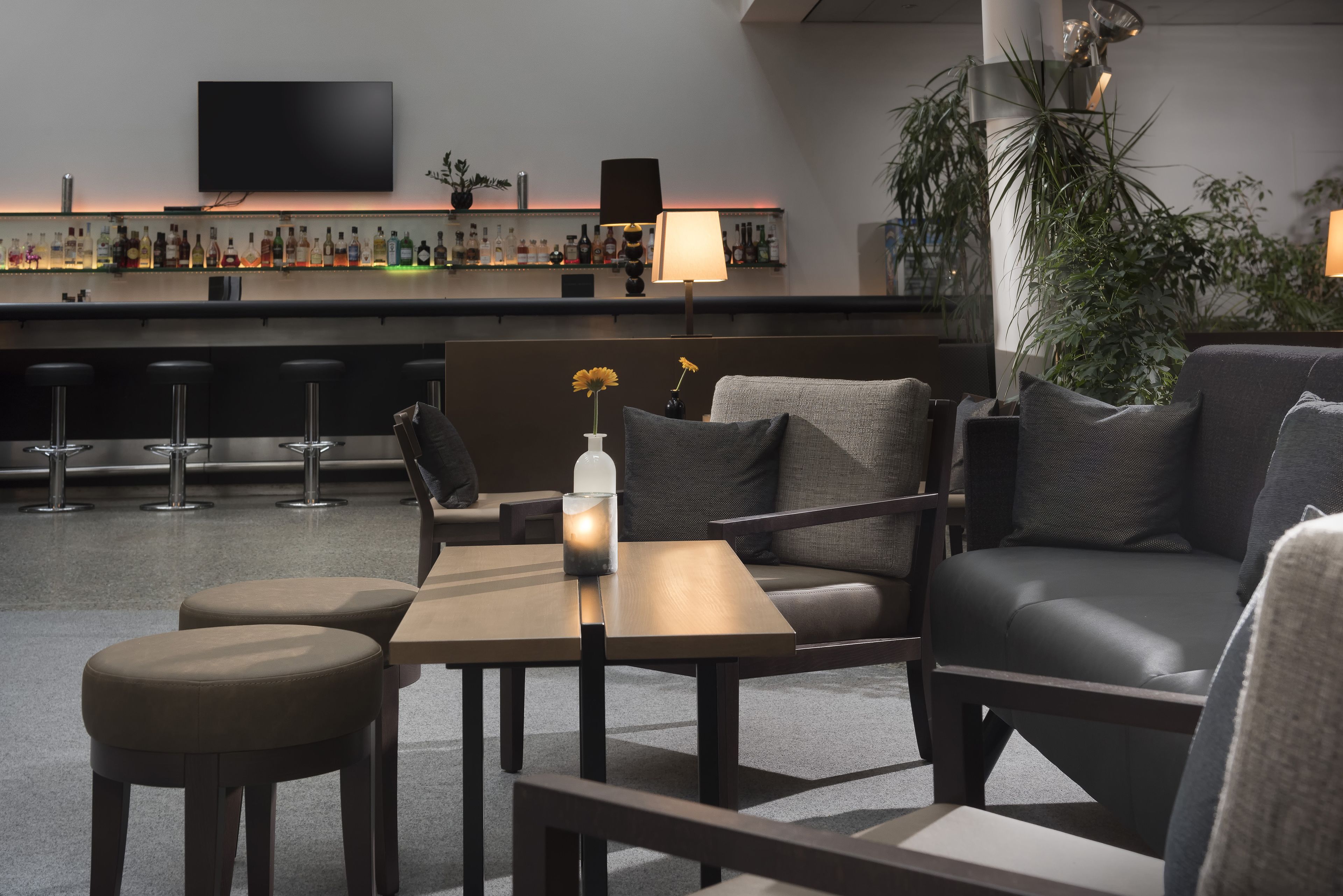 Un moderno espacio de bar con televisor de pantalla plana, taburetes, una variedad de botellas y una zona de estar cómoda con mesa y cojines.