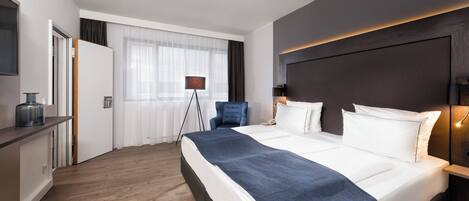 A hotel room with a bed, bedside table, lamp, and a view of the outside.