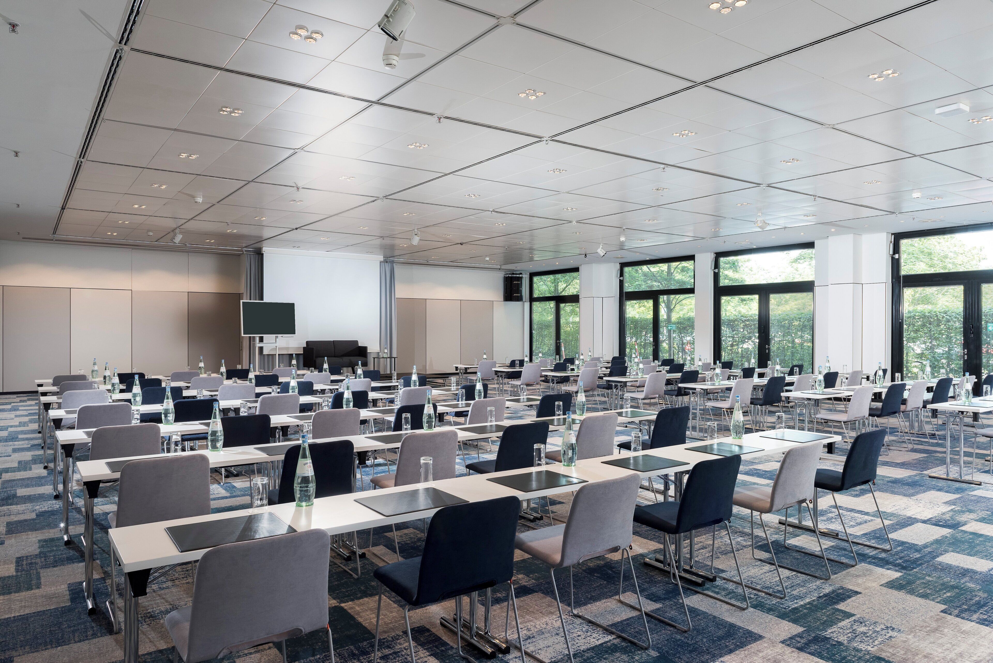 A large conference room with multiple tables and chairs, a flat-screen TV, and large windows.