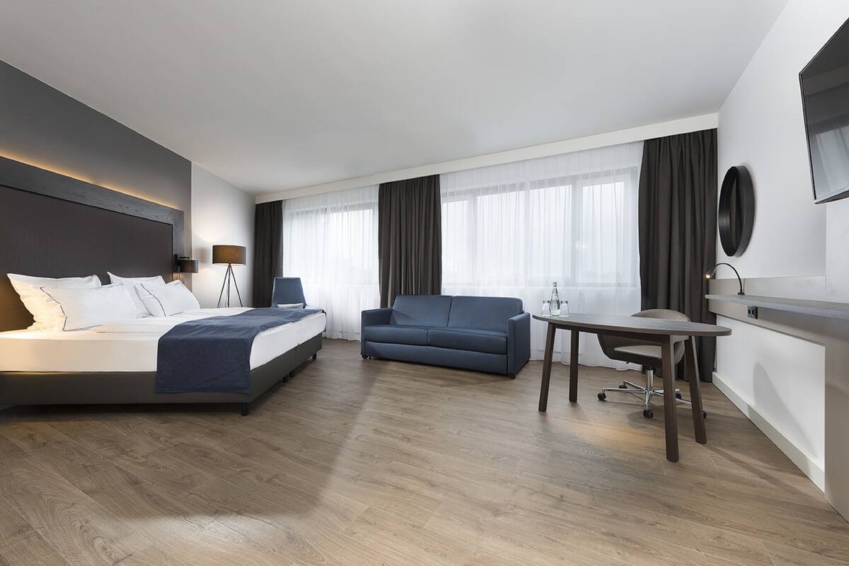 Una habitación de hotel moderna con cama, sofá, escritorio y televisión.