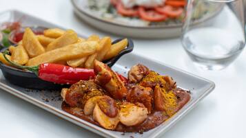 Hähnchen mit Gewürzen auf einem Teller, eine Schüssel Pommes und eine rote Chilischote.