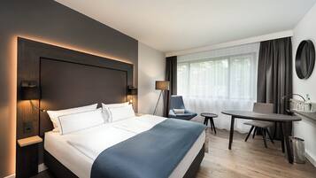 A hotel room with a large bed, a desk, a chair, a lamp, and a window with curtains.