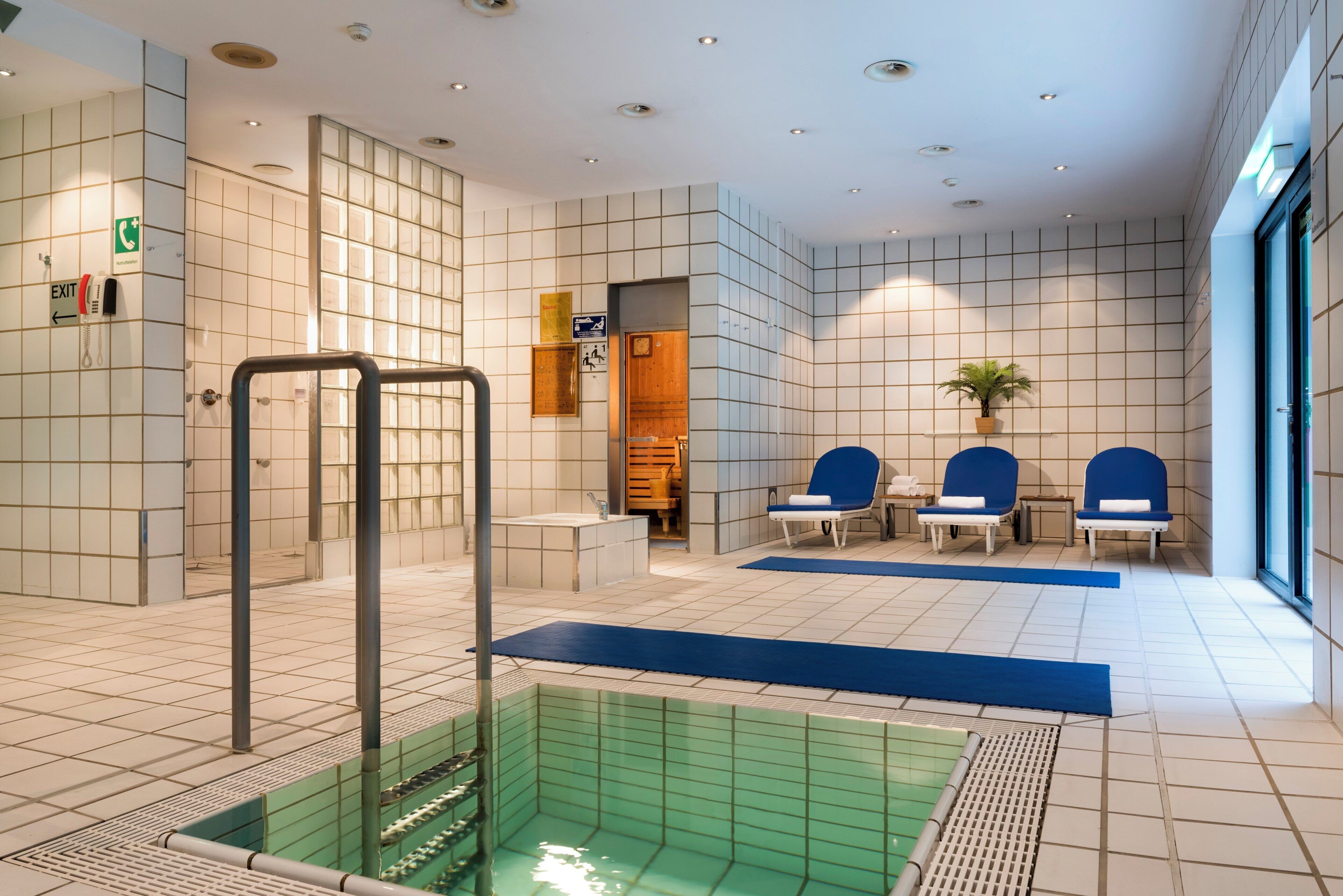 Un área moderna de piscina interior con un letrero de salida claro, un letrero de sauna y un mostrador de recepción.