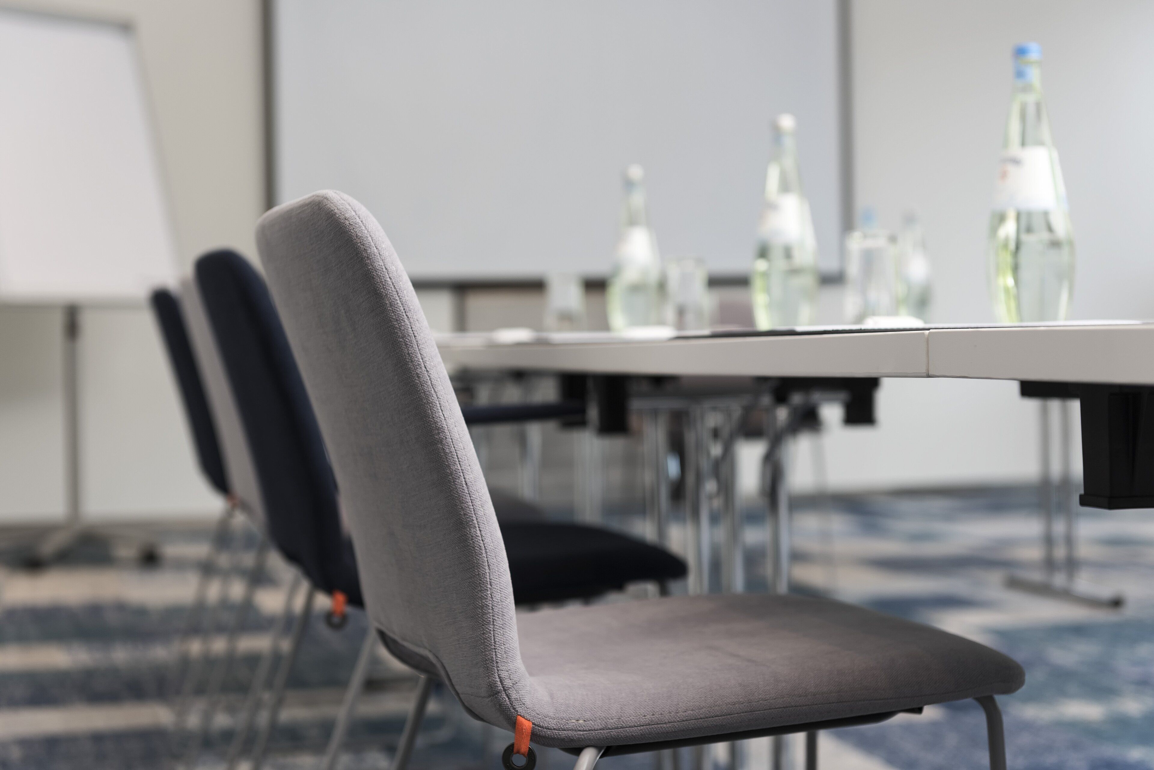 A conference room with a whiteboard, a table with water bottles, and two grey chairs.