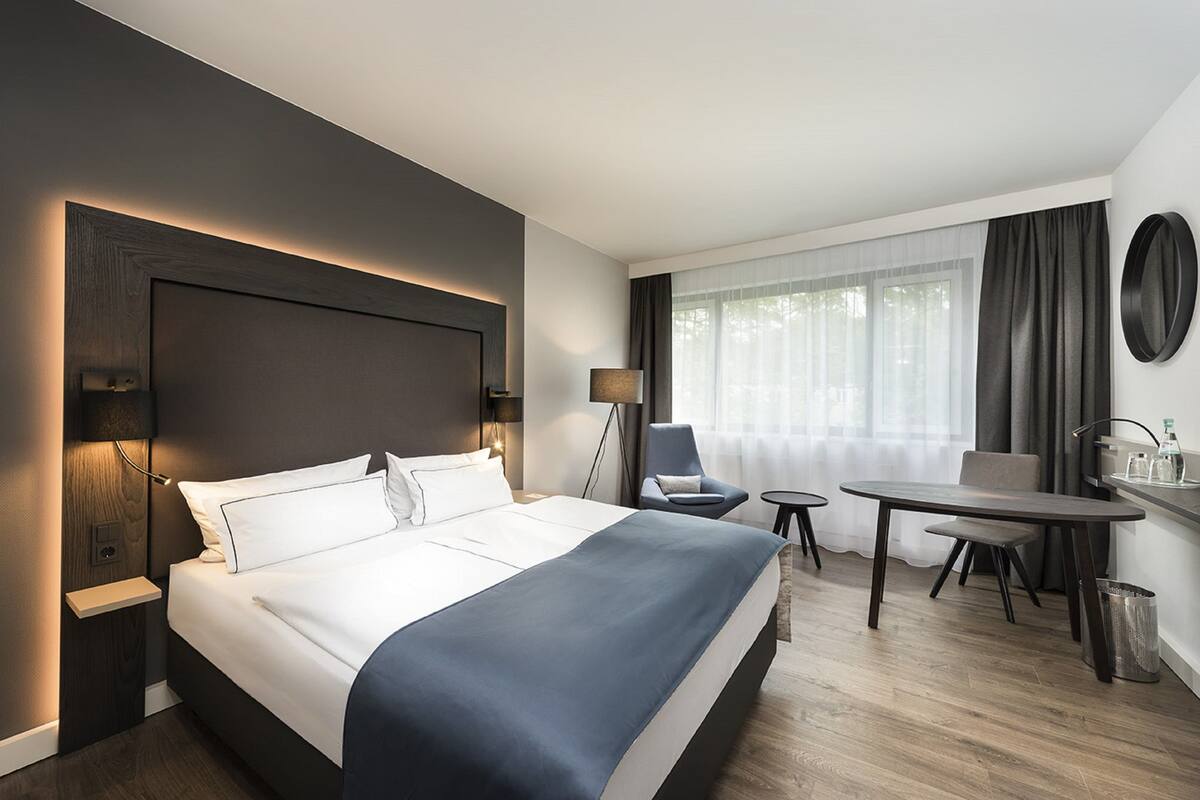 Una habitación de hotel moderna con una cama grande, mesitas de noche, un escritorio y una silla.
