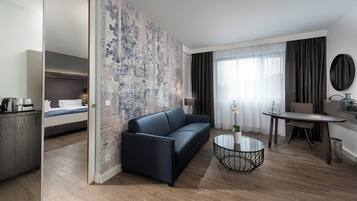A modern hotel room with a bed, a sofa, a dining table, and a coffee table.
