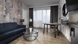 A modern living room with a dark blue sofa, a round glass coffee table, and a large abstract wall mural. - Holiday Inn Berlin City West by IHG (Berlin)