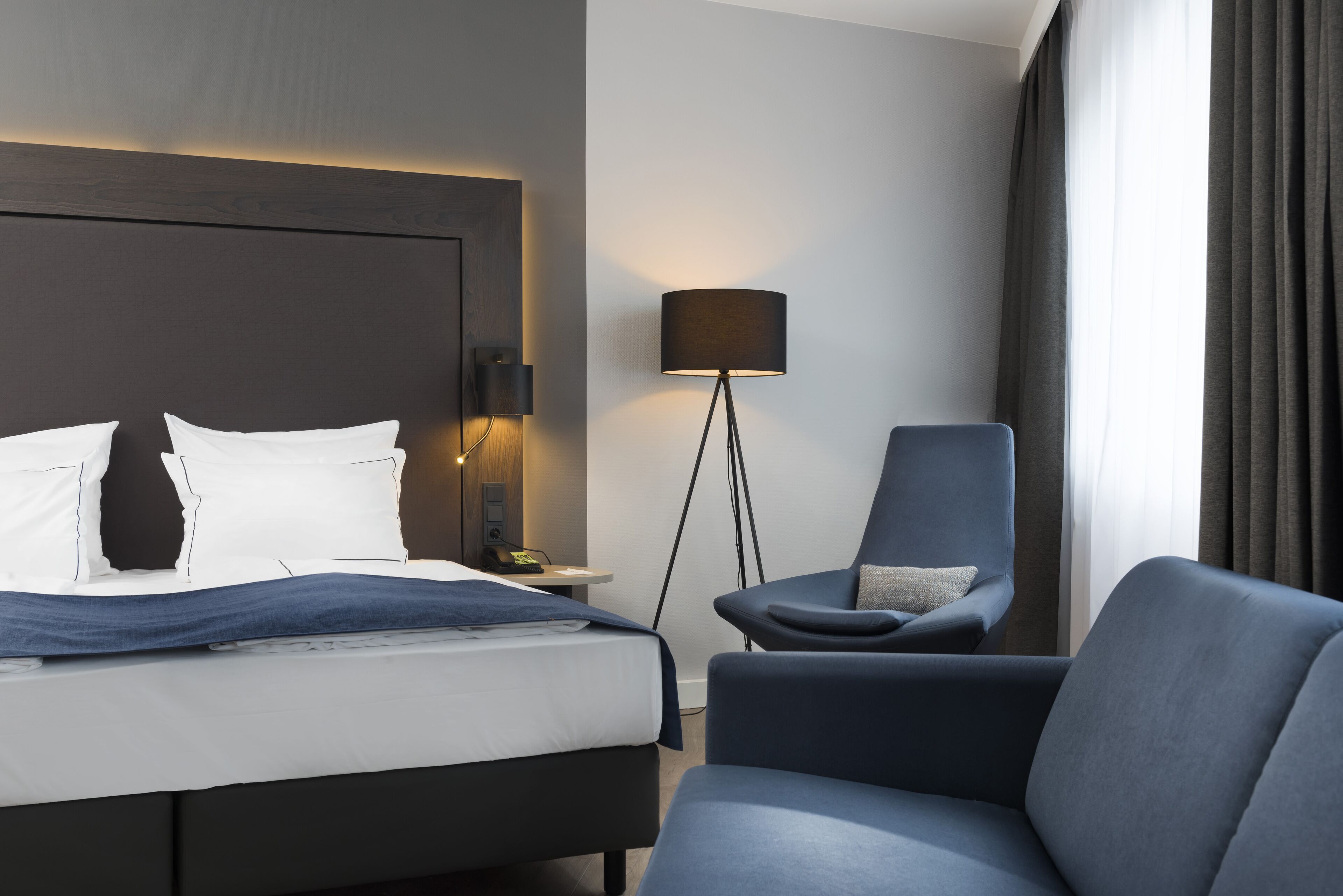 A hotel room with a bed, a chair, a lamp, and a view of the outdoors.