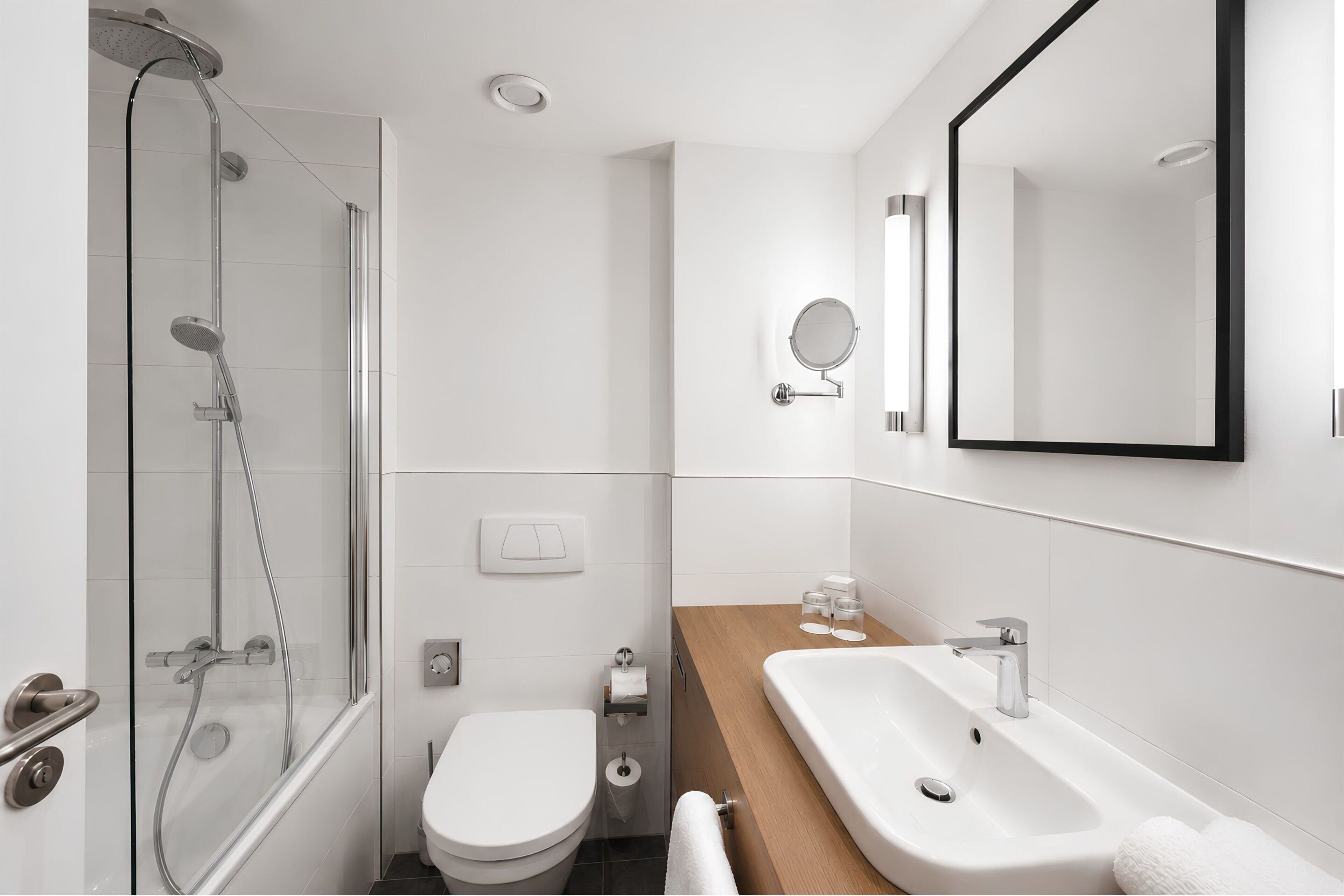 A modern bathroom with a glass-enclosed shower, a toilet, a sink, and a large mirror.