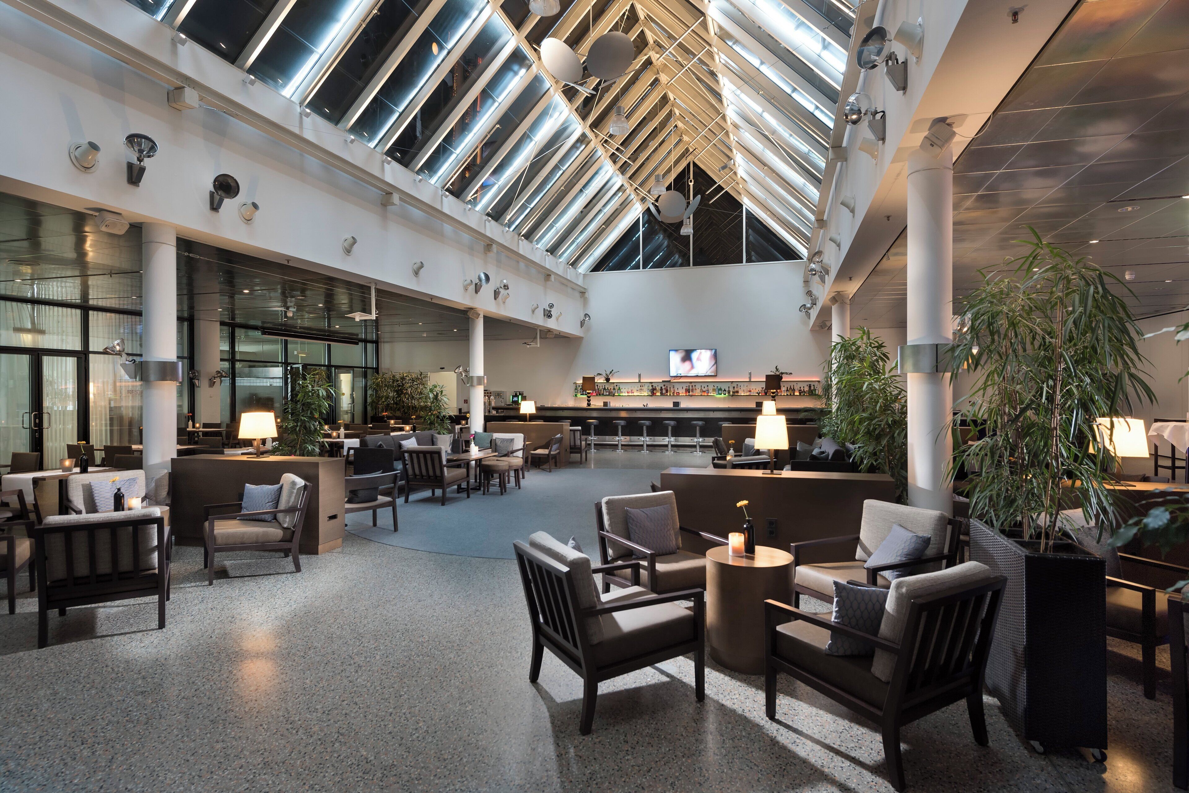 A spacious lobby with a high ceiling, large windows, and a bar area.