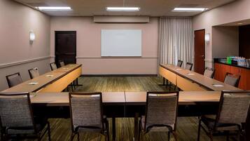 A conference room with a long table, chairs, a projector screen, and a water dispenser.