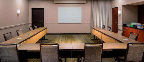 A conference room with a long table, chairs, a projector screen, and a water dispenser.