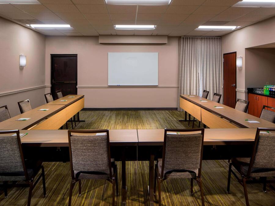 A conference room with a long table, chairs, a projector screen, and a water dispenser.