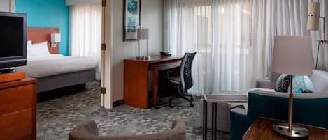 A hotel room with a bed, a desk, a chair, a TV, and a sofa.