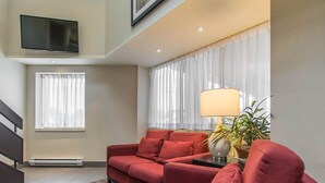 A modern living room with a red sofa set, a flat-screen TV mounted on the wall, and a large window with sheer curtains. - Comfort Inn Val-d Or (Val-d'Or)