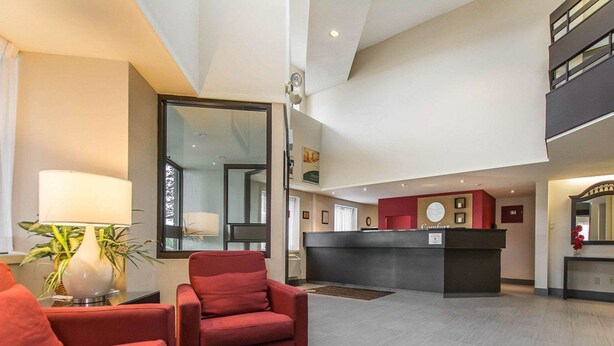 A hotel lobby with a reception desk, a red armchair, a sofa, and a lamp.