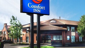 A Comfort Inn sign with a stylized sun logo, a brick building with a tiled roof, and a well-maintained lawn in front. - Comfort Inn Val-d Or (Val-d'Or)