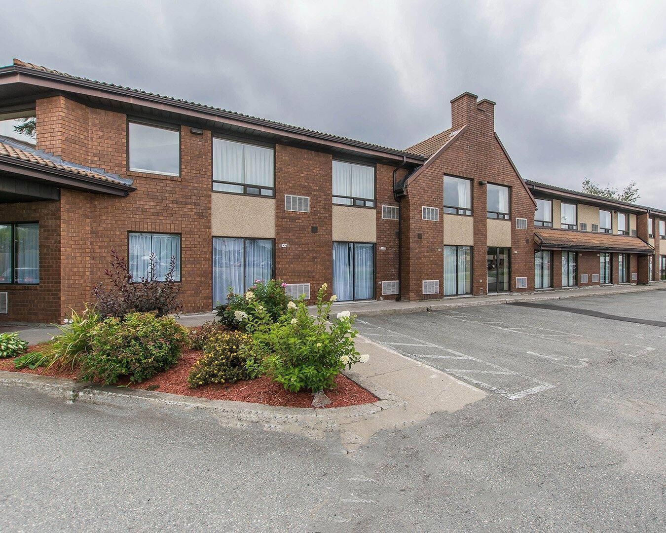 A row of brick buildings with large windows and a parking lot in front.