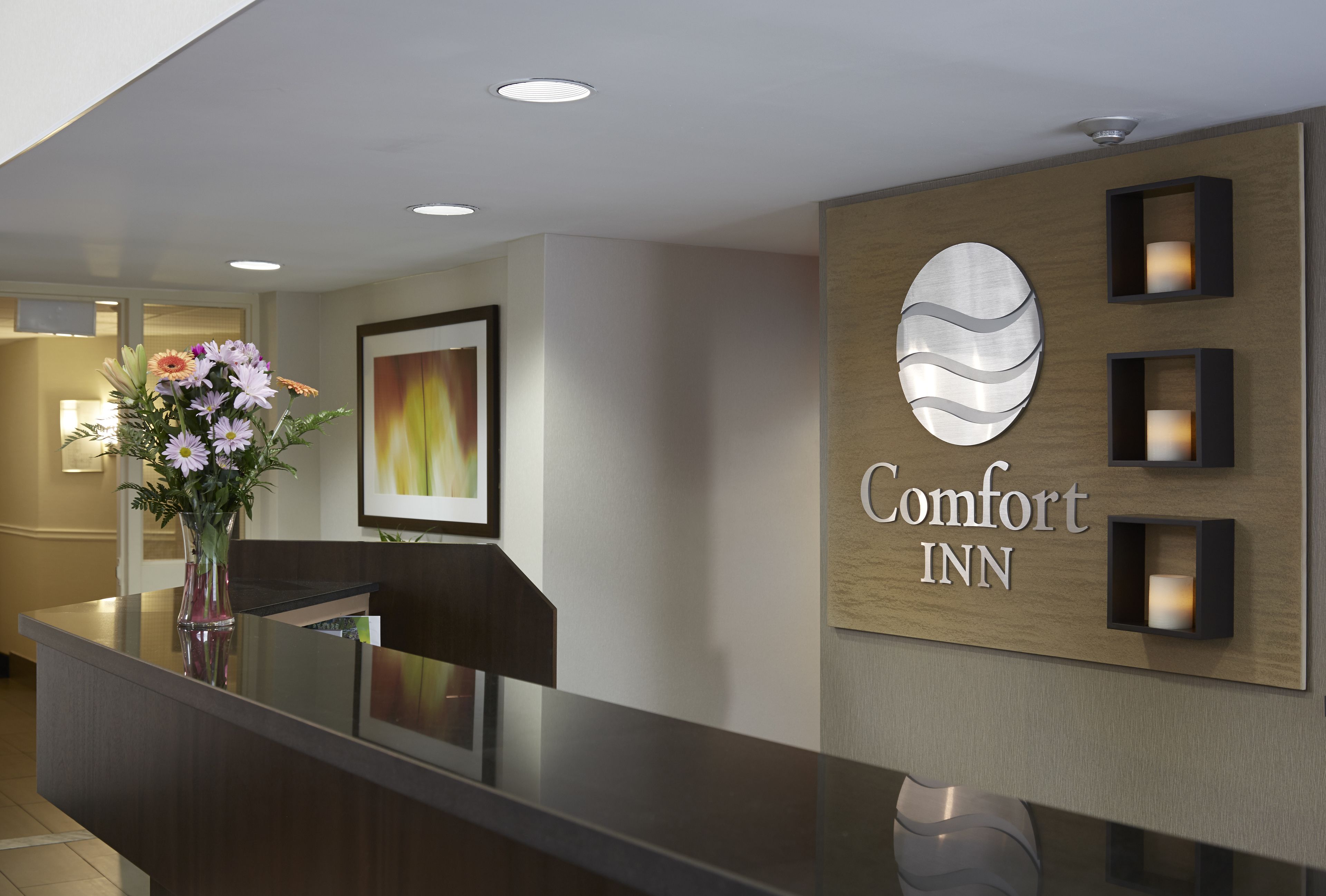A reception desk with a vase of flowers, a framed picture, and a sign for Comfort Inn.