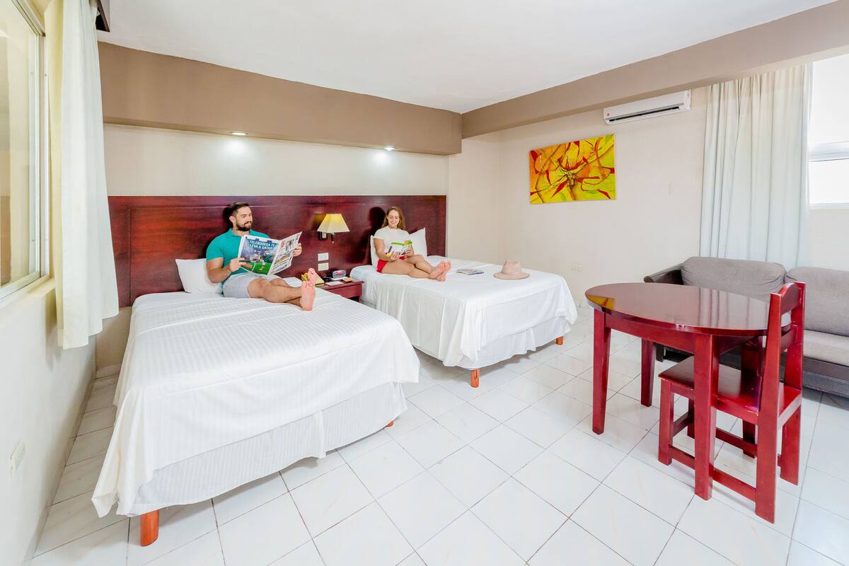 A hotel room with two beds, a dining table, and a sofa.