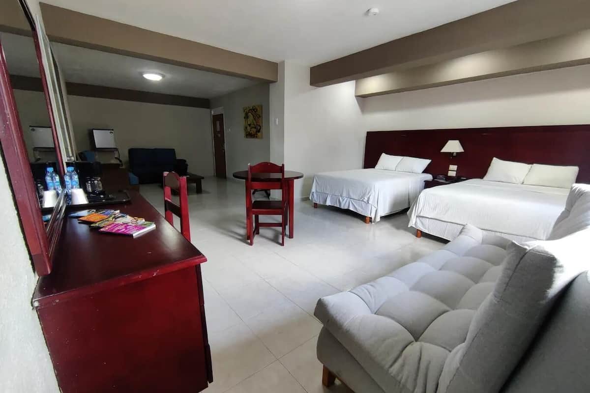 A hotel room with a desk, two beds, a sofa, and a dining table.