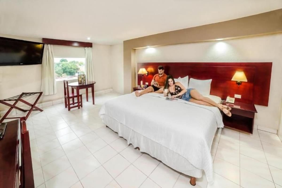 Una habitación de hotel con una cama grande, mesitas de noche, un escritorio y una televisión.