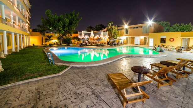 A swimming pool with lounge chairs and umbrellas, surrounded by a building with multiple floors and balconies. - Hotel Maria del Carmen Merida (Mérida)
