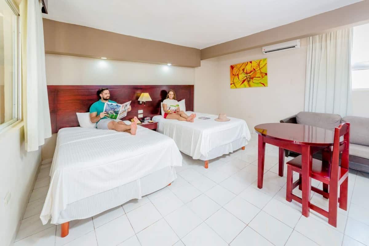 A hotel room with two beds, a small table, and a sofa.