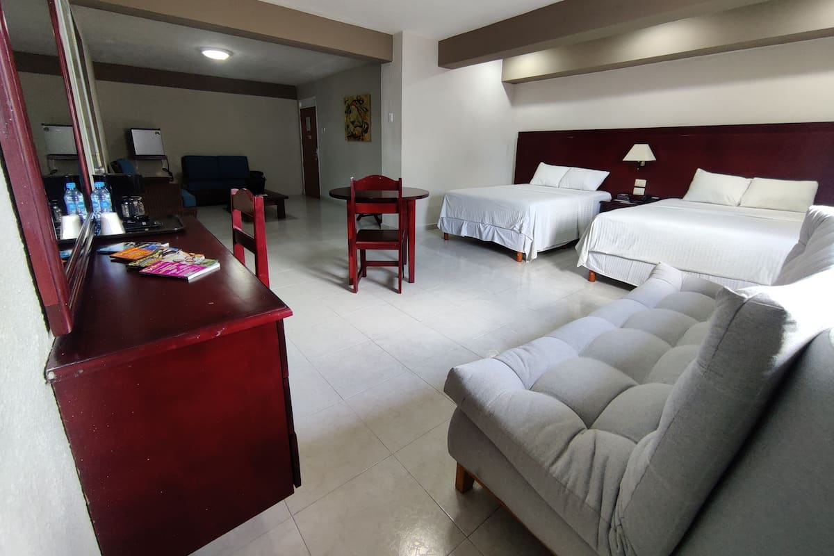 A hotel room with a desk, two beds, a sofa, and a dining area.