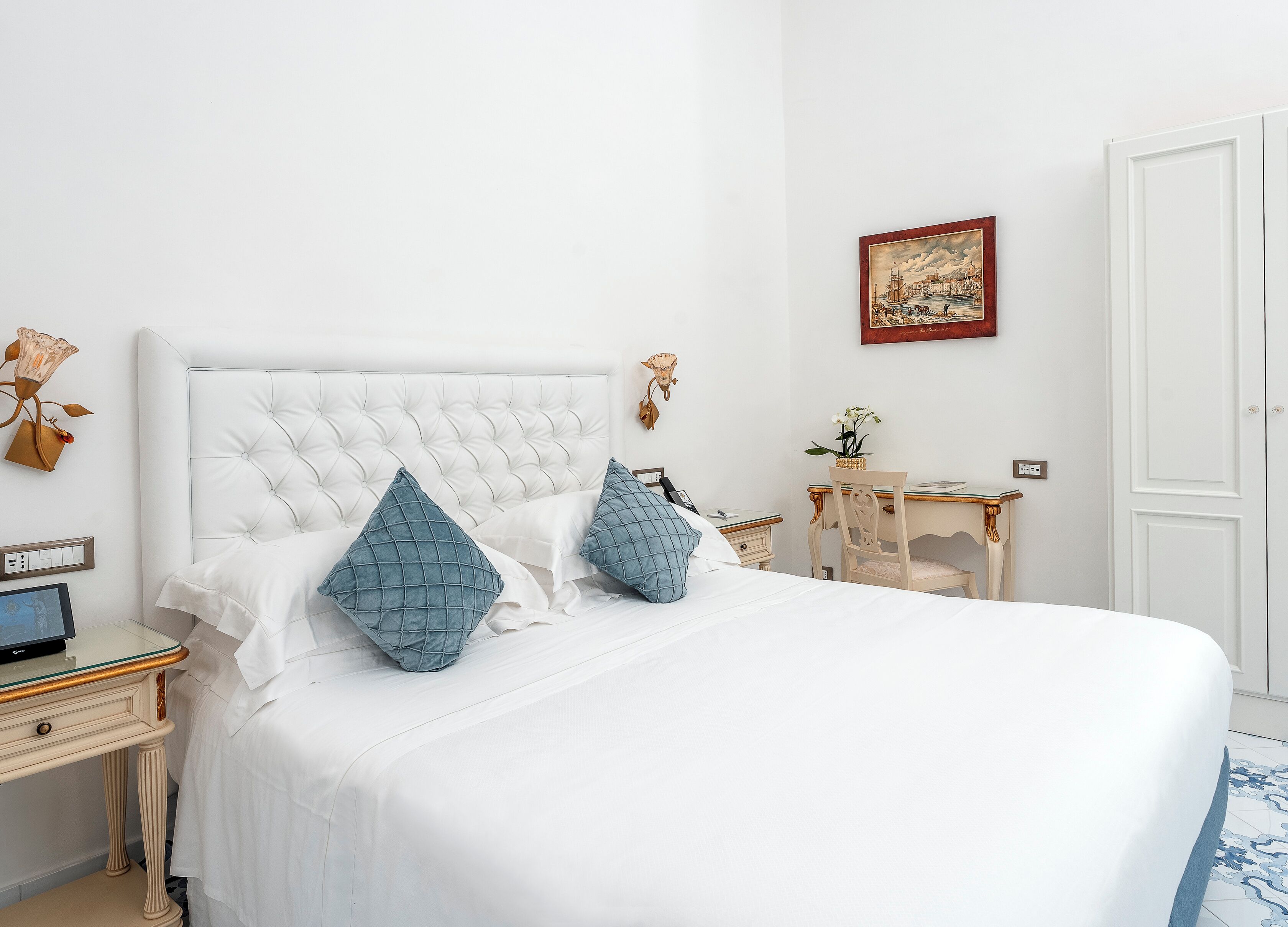 A neatly arranged bedroom with a large bed, a bedside table with a lamp, a small desk, and a chair.