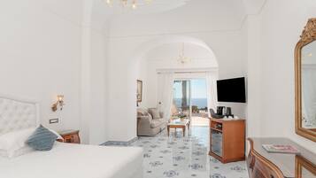A spacious bedroom with a large bed, a desk, and a view of the sea.