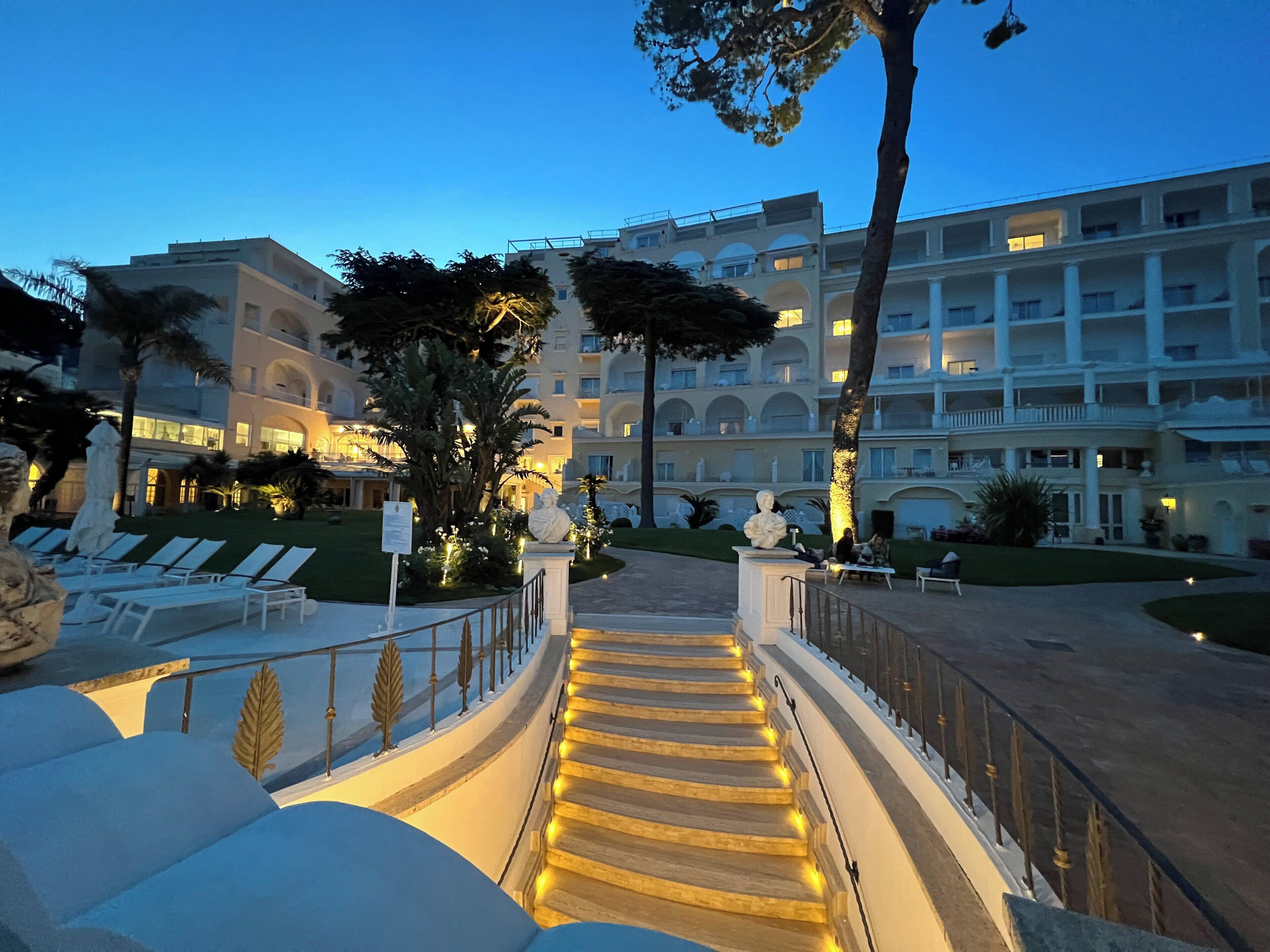 Un hotel con una escalera monumental, sillones de descanso y un patio bien iluminado.