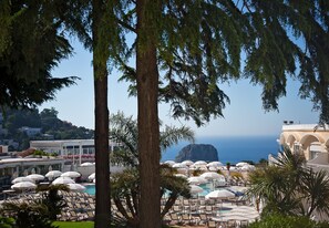 A resort with a pool area, lounge chairs, umbrellas, and a view of the sea.