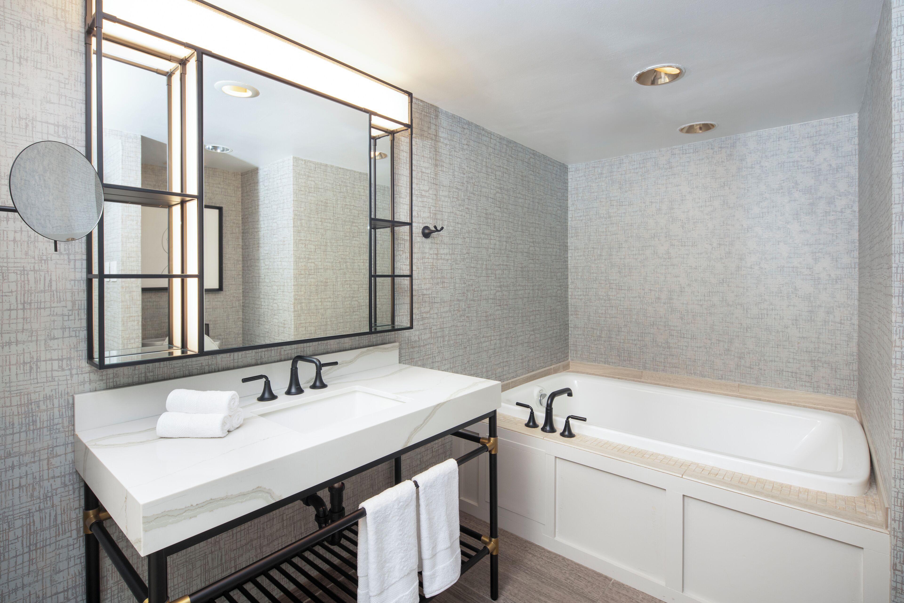 A modern bathroom with a large mirror, two sinks, a bathtub, and a towel rack.