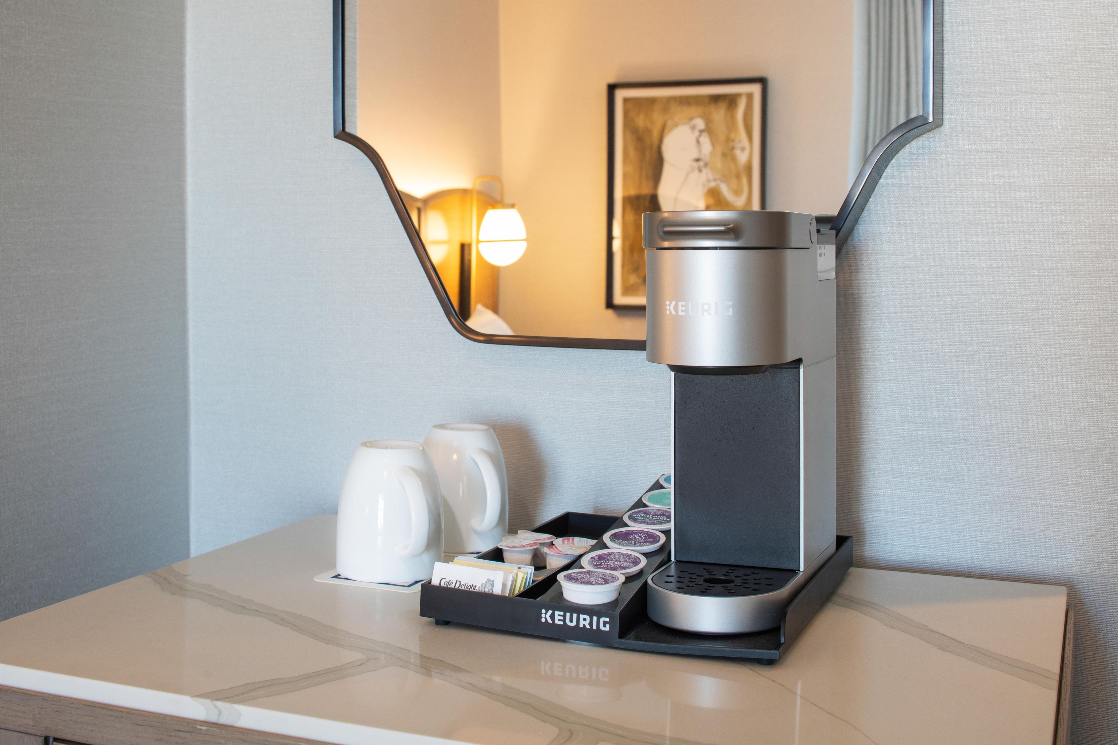 Una cafetera Keurig sobre una encimera, con una taza de café, una caja de cápsulas de café y una bandeja de cápsulas.