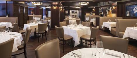 A restaurant with round tables set for dining, featuring chandeliers and wooden paneling.