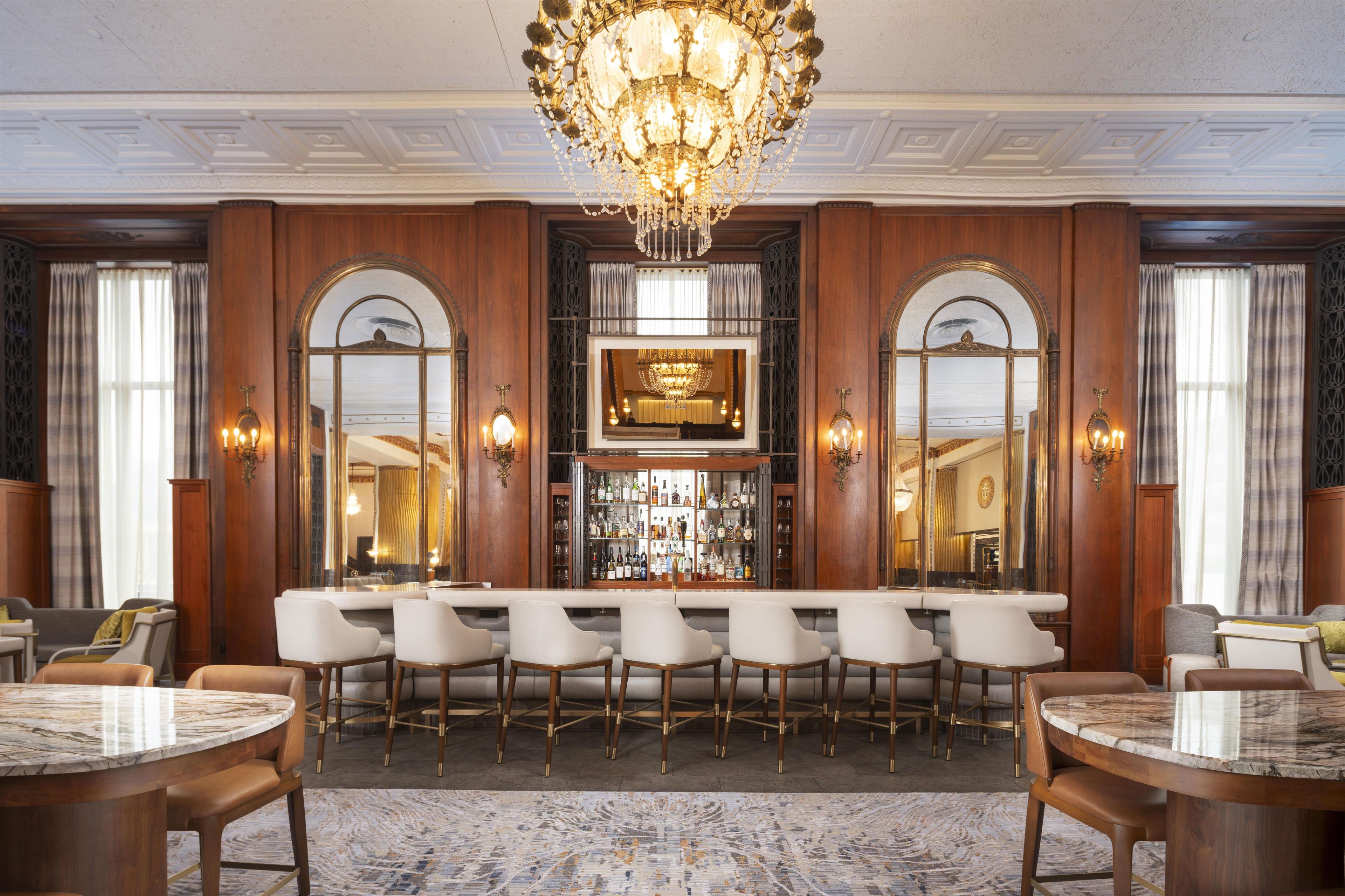 A bar area with a marble countertop, multiple bar stools, and a chandelier.