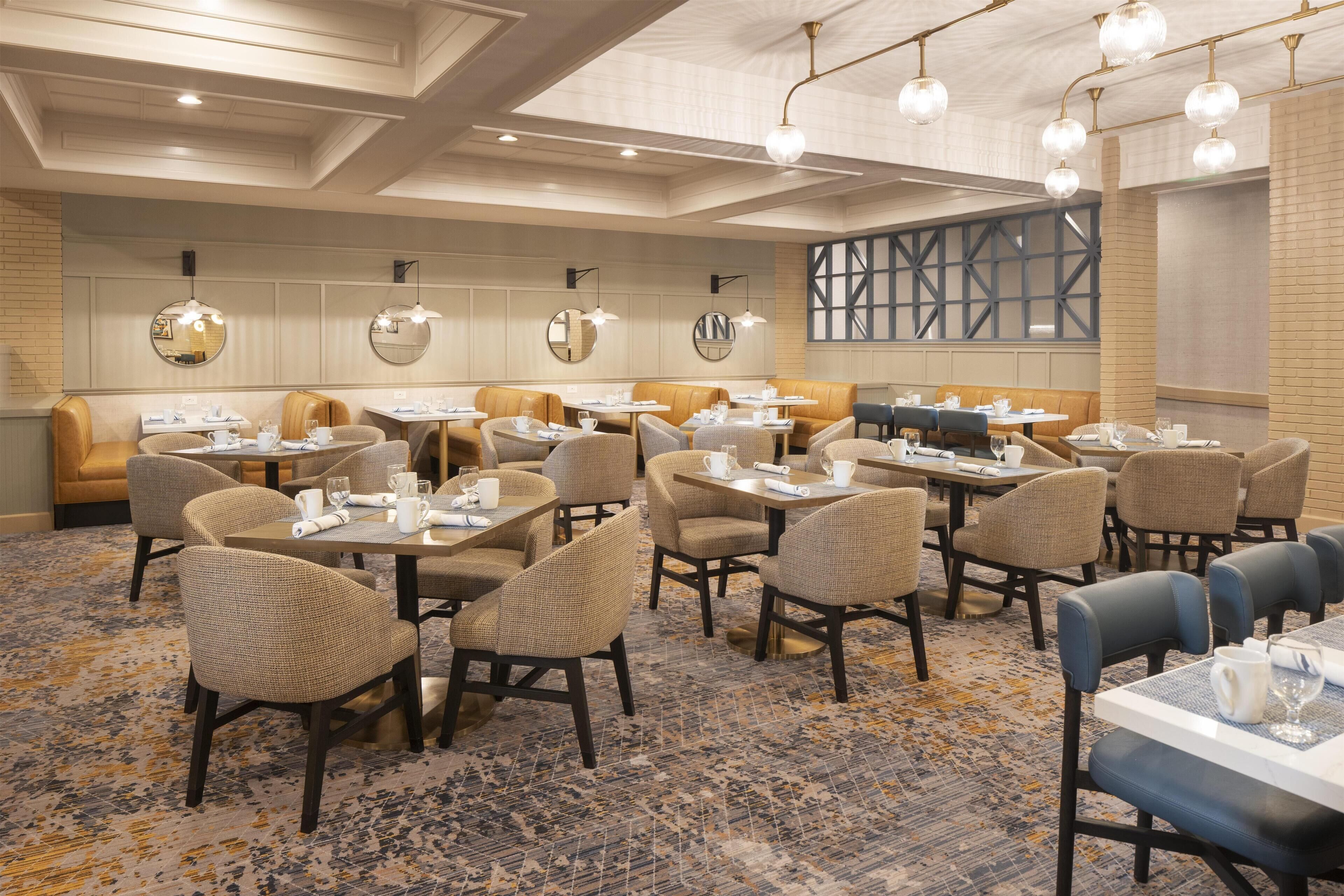 A restaurant with round tables and cushioned seating, featuring a patterned carpet and pendant lighting.